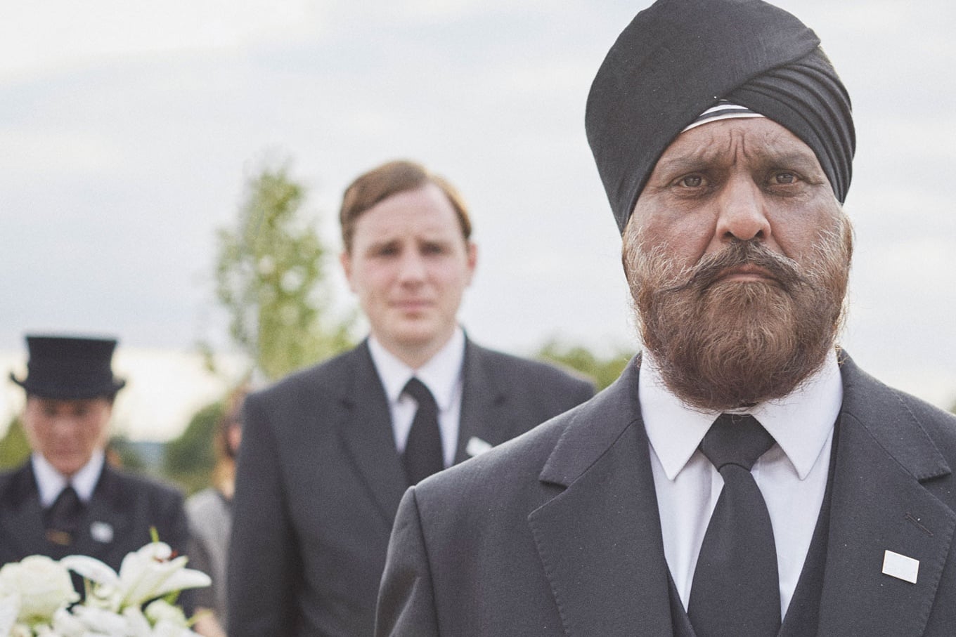 A Sikh funeral director wearing a turban helps to bear a coffin for a traditional funeral